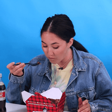GIF of woman eating from box of poutine grossed out