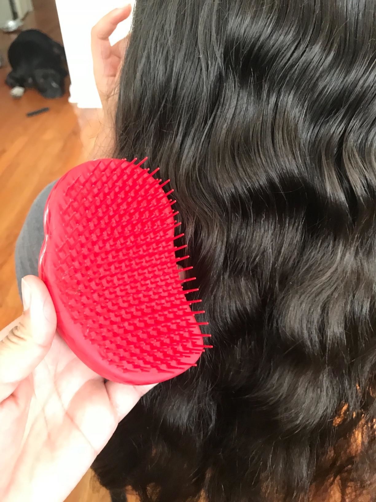 hand holds red Tangle Teeser brush in front of neatly-combed thick wavy hair