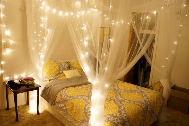 the white sheer canopy hanging over a bed with fairy lights