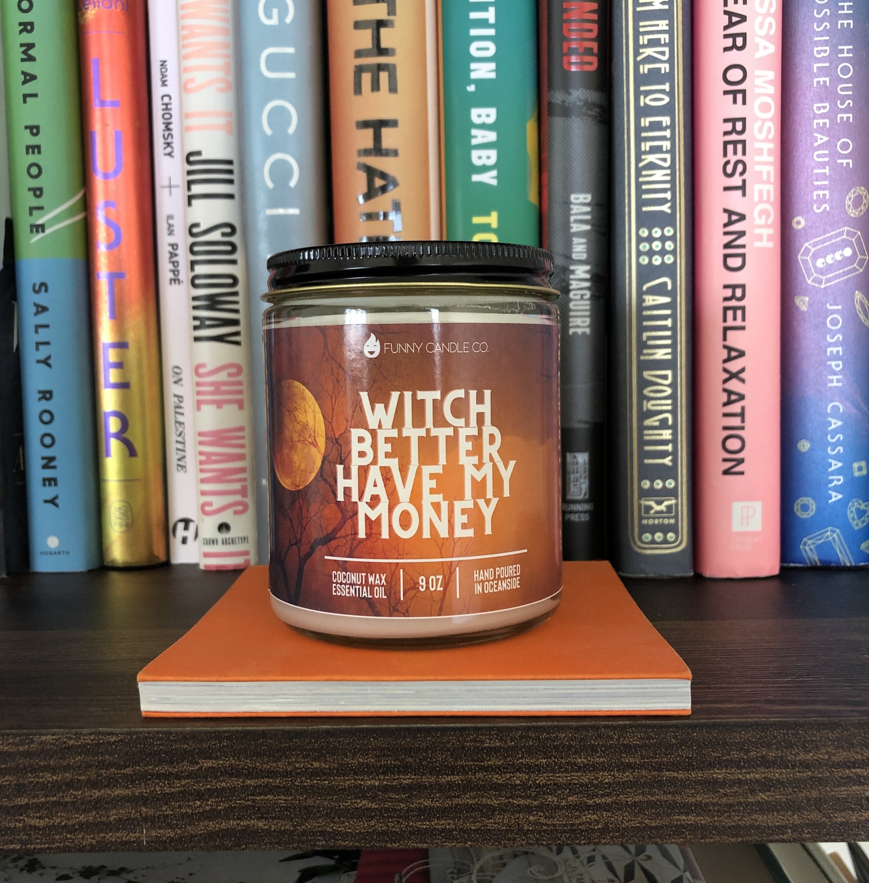 The candle reading &quot;witch better have my money&quot; is displayed on a bookshelf