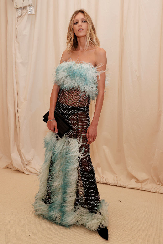 Anja Rubik wearing a sparkly mesh ensemble with feathers covering the neckline and some more placed mid-thigh to the floor