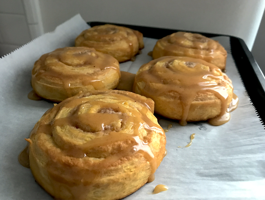 Five pumpkin cinnamon rolls on a baking sheet, covered in pumpkin spice glaze