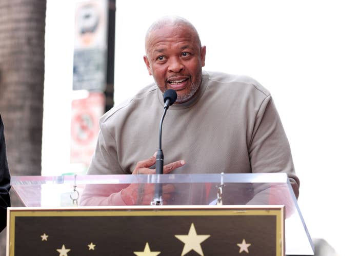 Dr. Dre speaks at a podium outside while pointing at his chest
