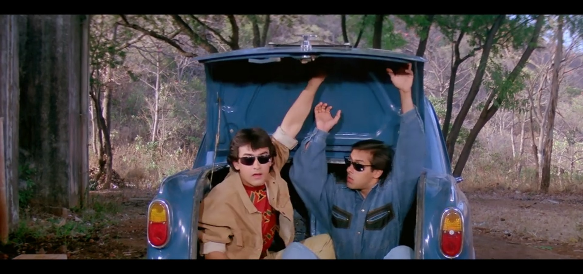 Amar and Prem coming out of the trunk of a blue car