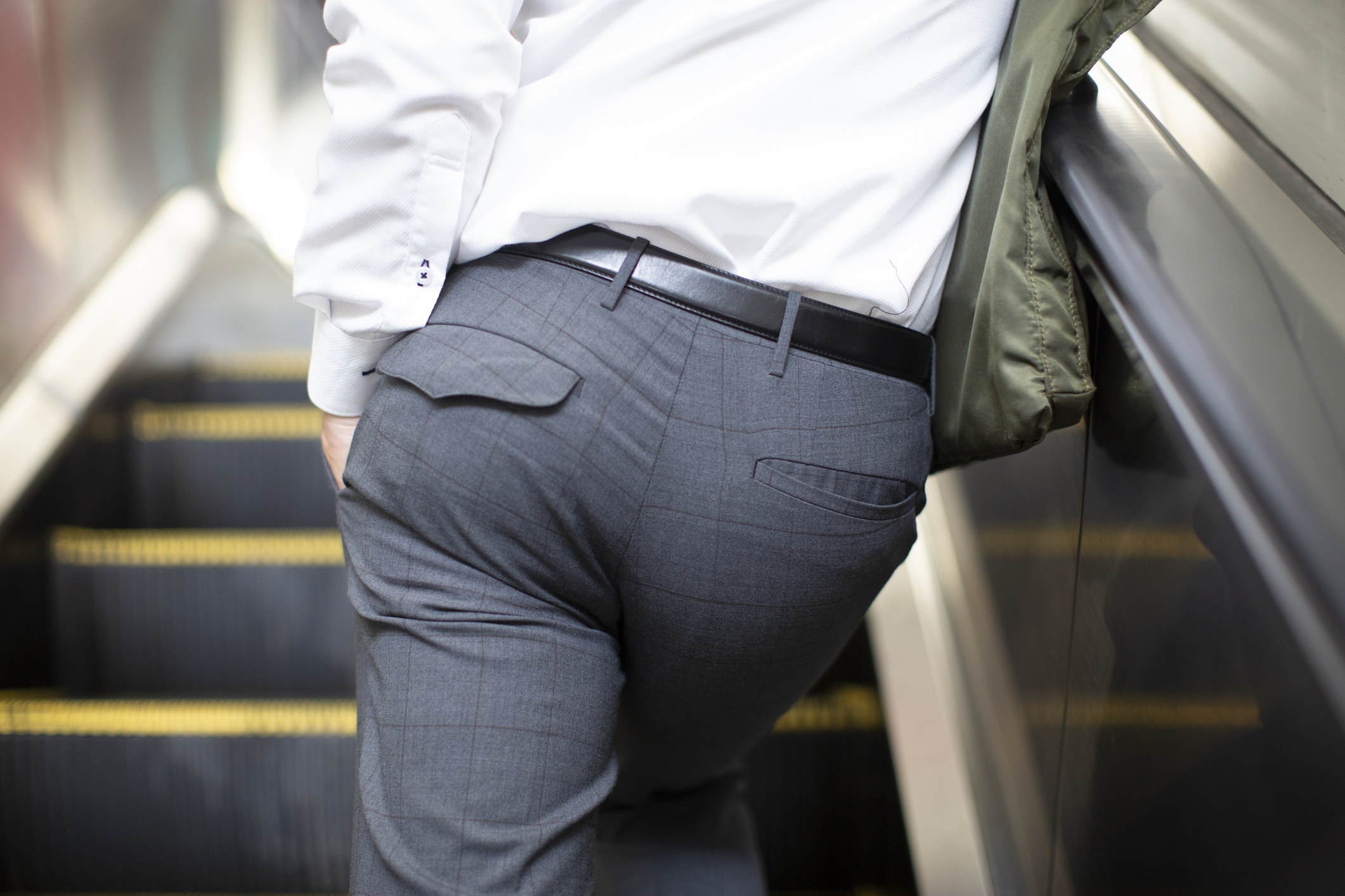 A man standing on a escalator with a closeup of his butt