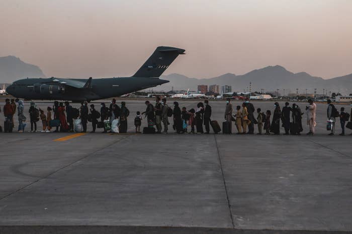 A long line of people stand on an airfield