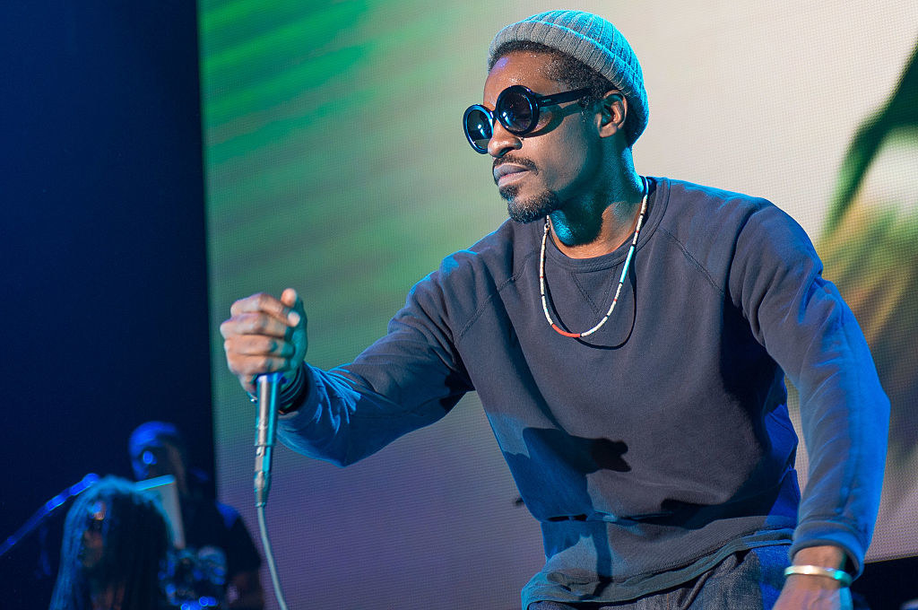 Andre performing on stage in a long-sleeved shirt, beanie, and sunglasses