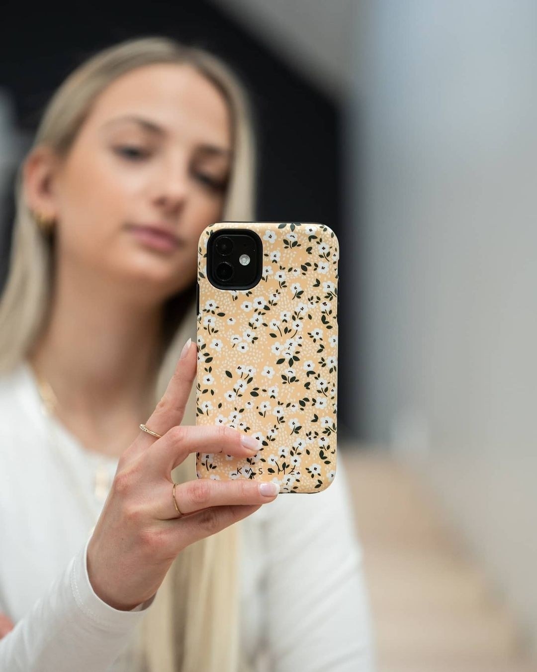 A person holding a phone with with a hard case that has a floral illustration on it