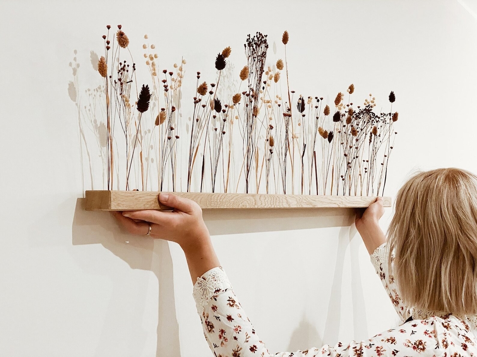 natural wood mounted shelf with stems of different dried flowers placed upright on top