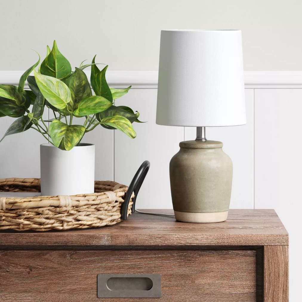 A olive/cream, ceramic table lamp with a white shade