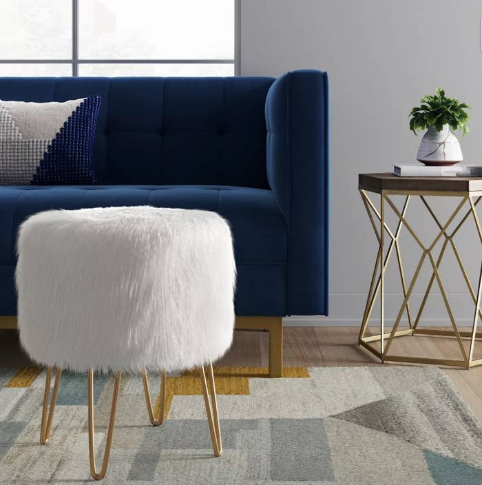 A white, fur, round ottoman with gold legs in a living room