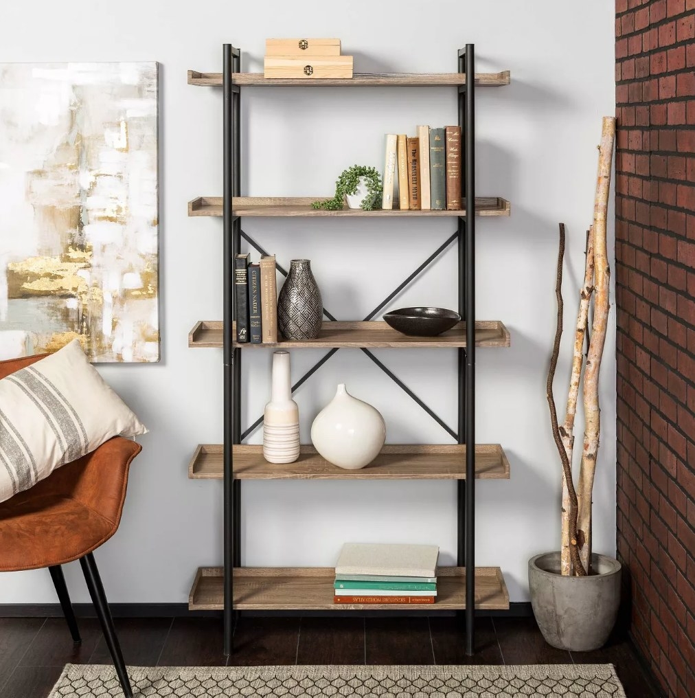 A metal/driftwood, 5-tier bookshelf filled with books, vases, and other decorative pieces