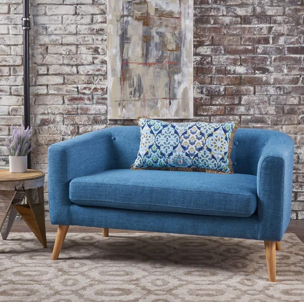 A mid-century modern, muted blue, loveseat with a throw pillow atop