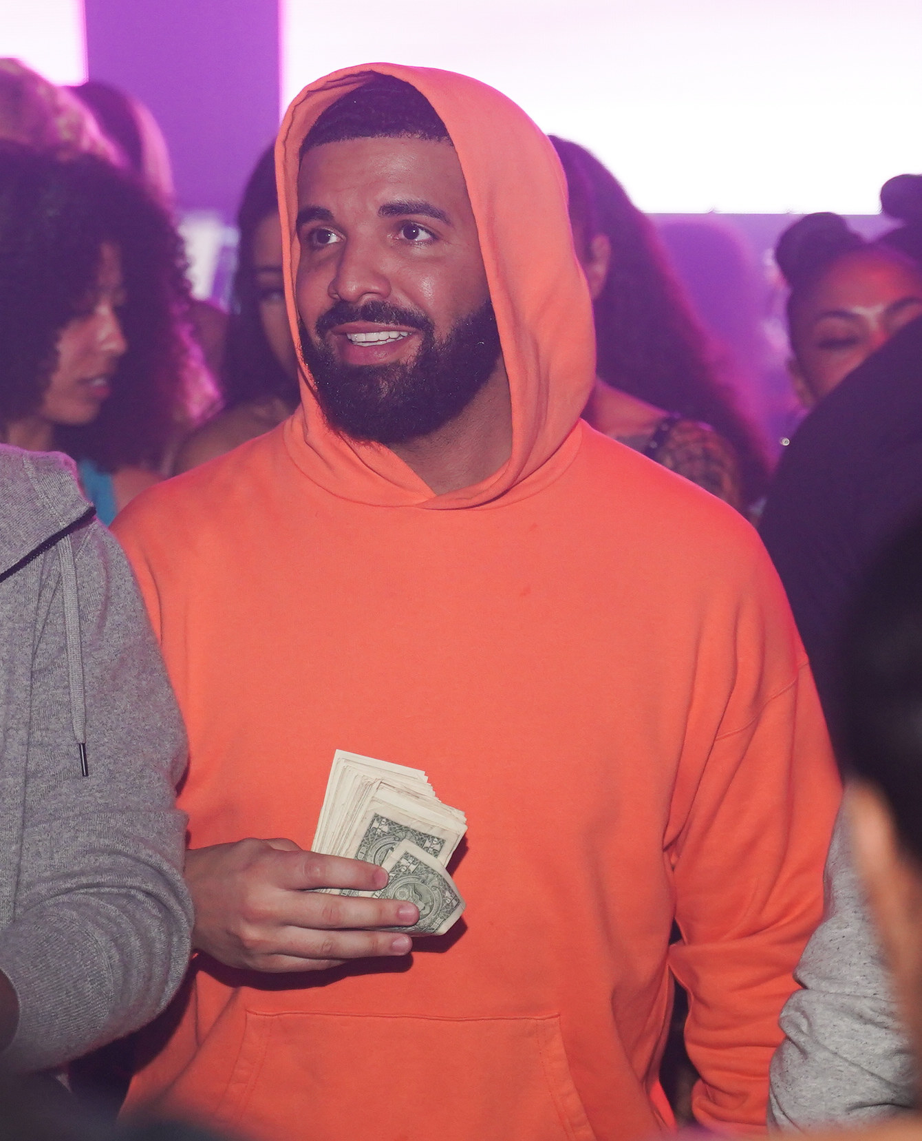 Drake in a hoodie and holding a roll of bills