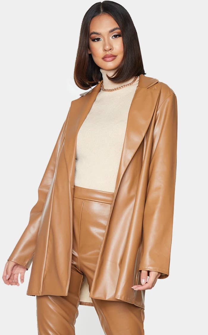 model wearing tan jacket over a cream turtle neck, chain link necklace, and matching faux leather pants