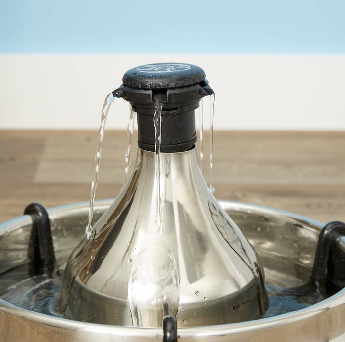 The silver fountain has a black top that spouts out water on all sides