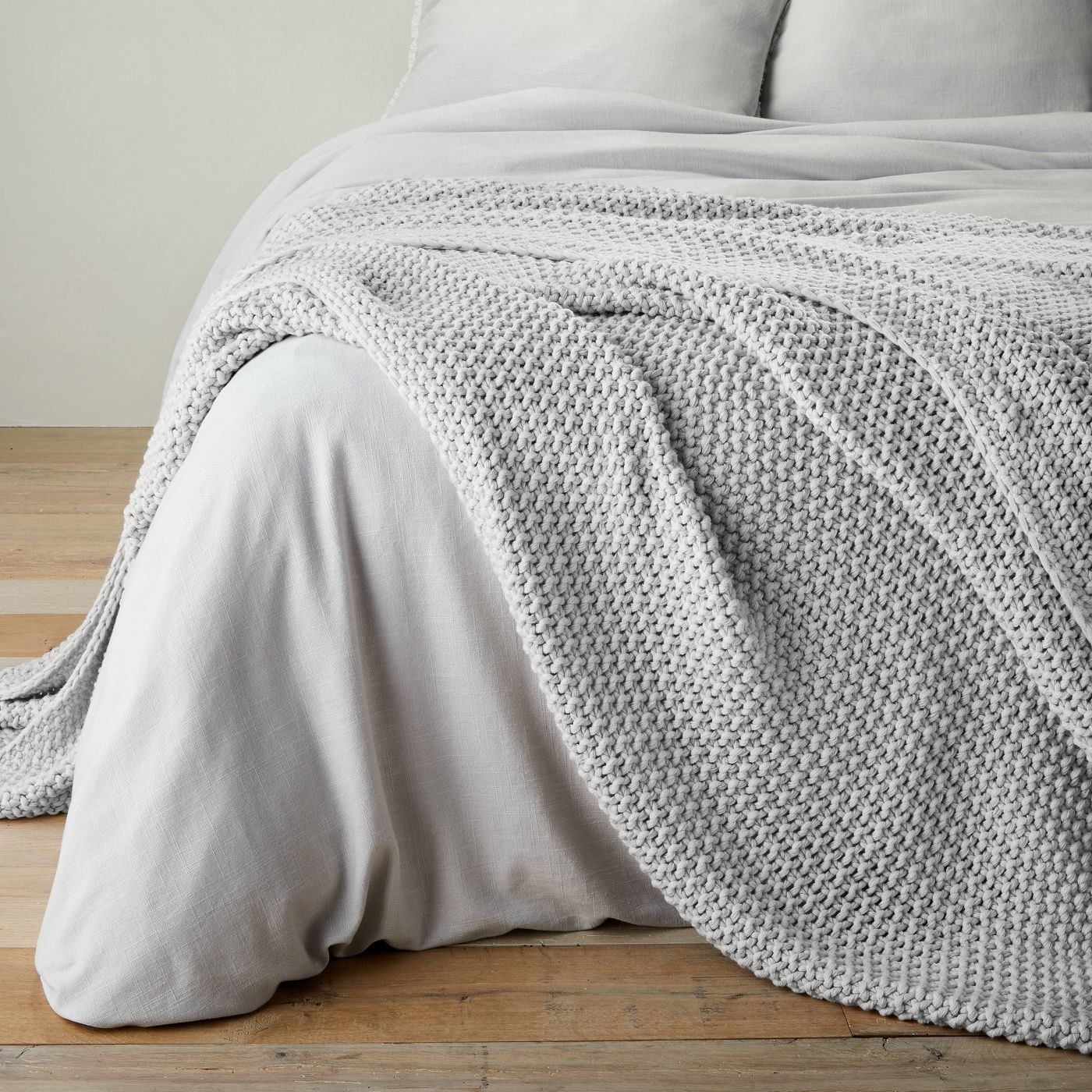 light grey chunky knit blanket draped on a bed