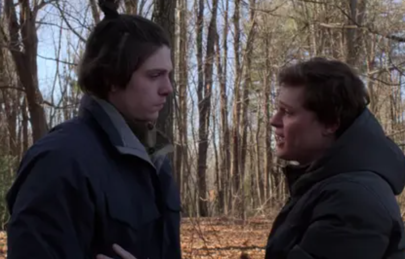 Grizz looks down towards Sam as Sam is mid sentence while they&#x27;re standing in the woods