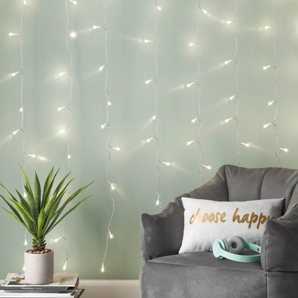 LED string lights hanging on the wall in a living room with an accent couch and planter in front