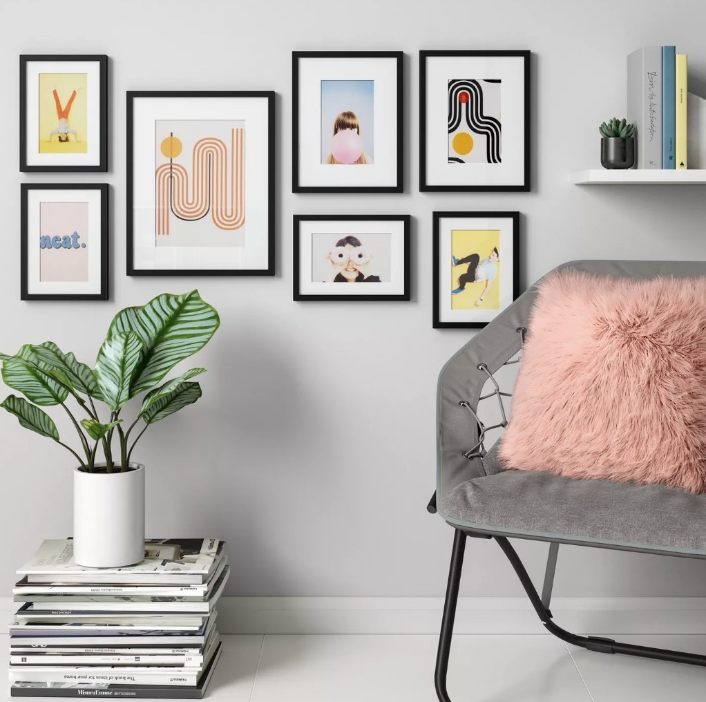 A set of 7, black frames hanging on a wall with a chair and planter in front