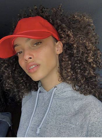 Model in a red baseball hat with room in the back for their curls 