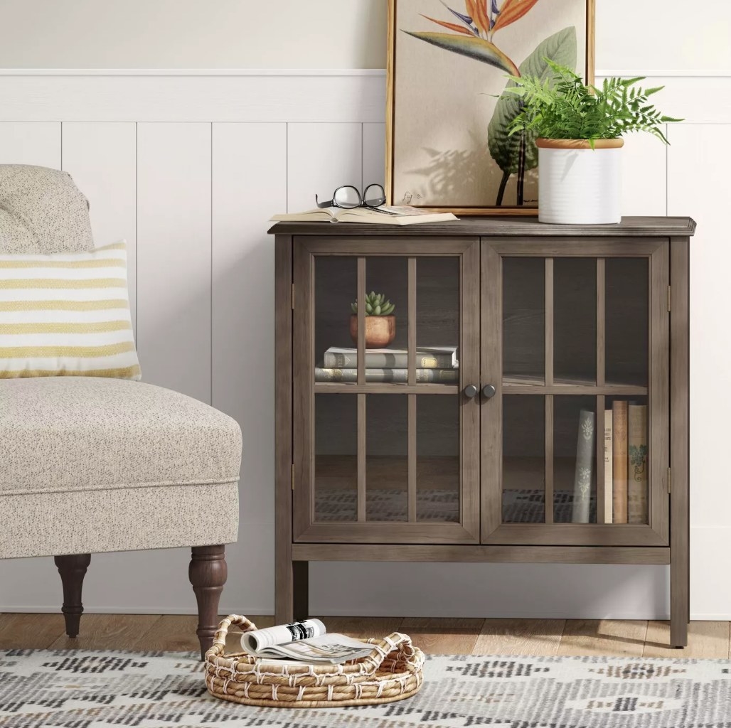 A brown, 2 glass doored storage cabinet next to an accent chair in a living room