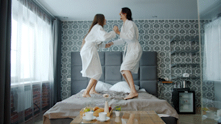 couple in robes jumping on their hotel bed