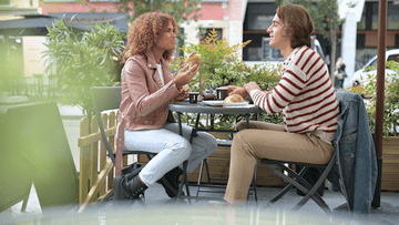 couple at a cafe, woman giving man croissant to try