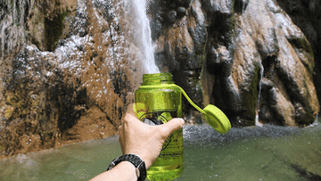 open reusable water bottle being filled up by a water fall