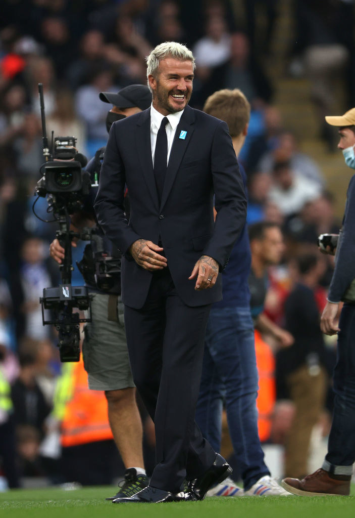 Smiling at a soccer game, but wearing a suit, not a uniform