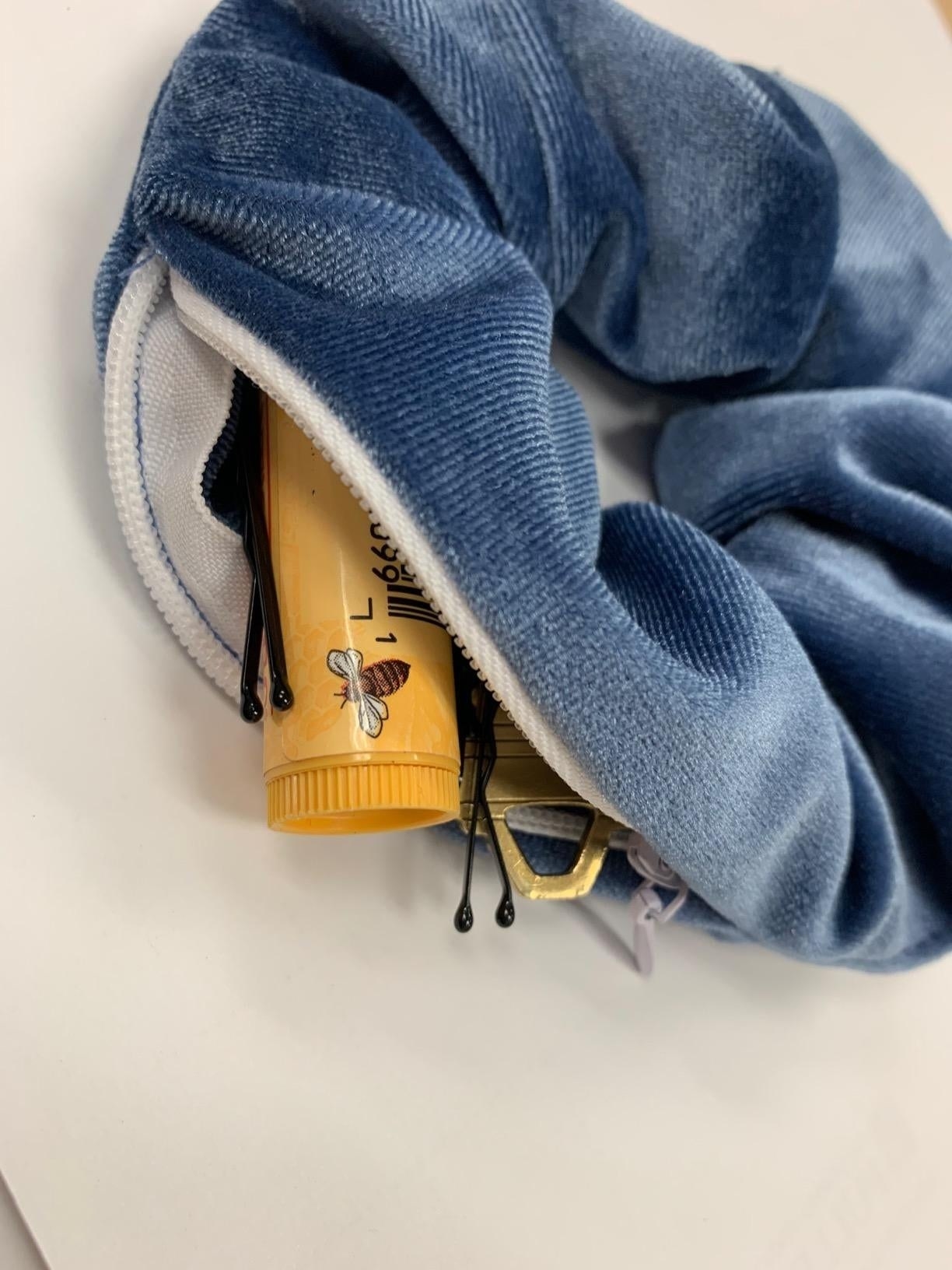 lip balm, pins, and other small items inside a reviewer's blue velvet scrunchie with zipper 