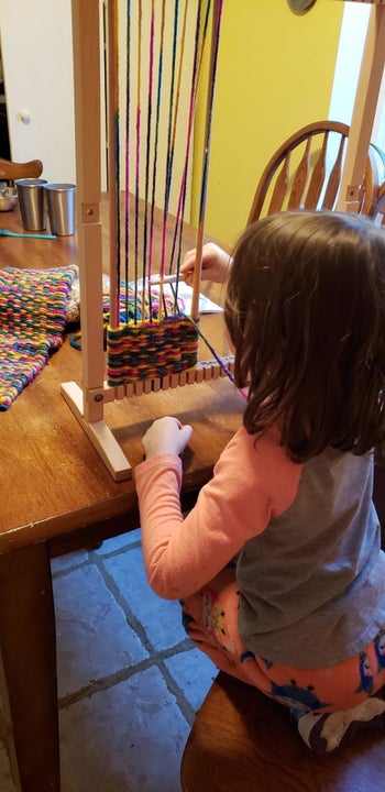 Reviewer's child inserting the wooden needle through the multicolored threads on the loom