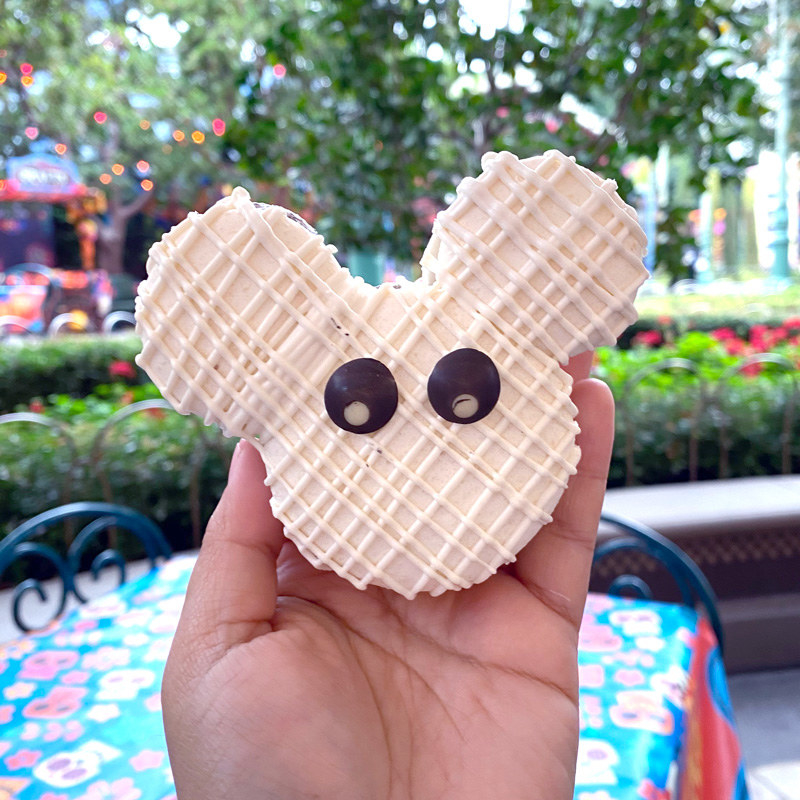 A macaron in the shape of mickey&#x27;s head, covered in vanilla frosting that&#x27;s strung across to look like mummy bandages