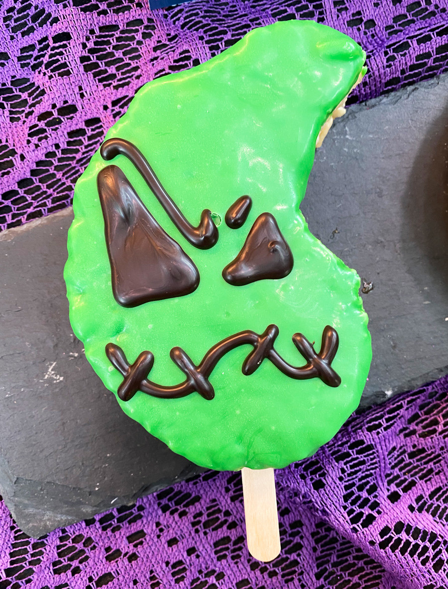 A rice krispies treat in the shape of Oogie Boogie&#x27;s head, with thick frosting and his face with stitched mouth, and eyes of different sizes