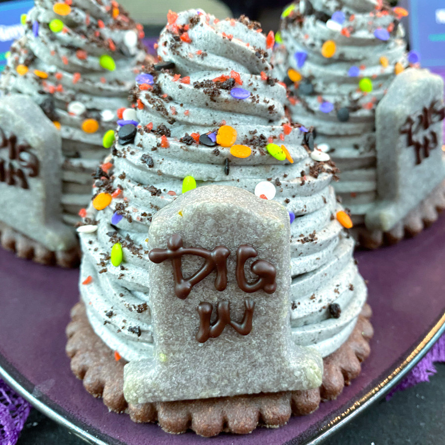 A swirl of grey mousse on top of a round cookie, and an cookie on top of it all in the shape of a tombstone that says &quot;dig in&quot;