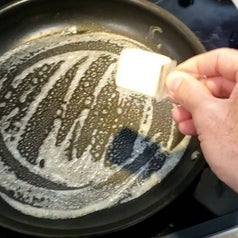 hand using the tool to butter a pan