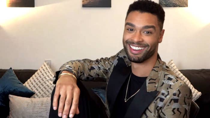 Regé-Jean Page smiling as he sits on a couch