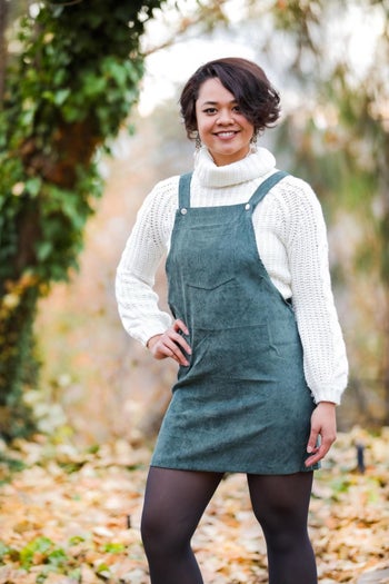 reviewer wearing the pinafore in green with a white turtleneck underneath