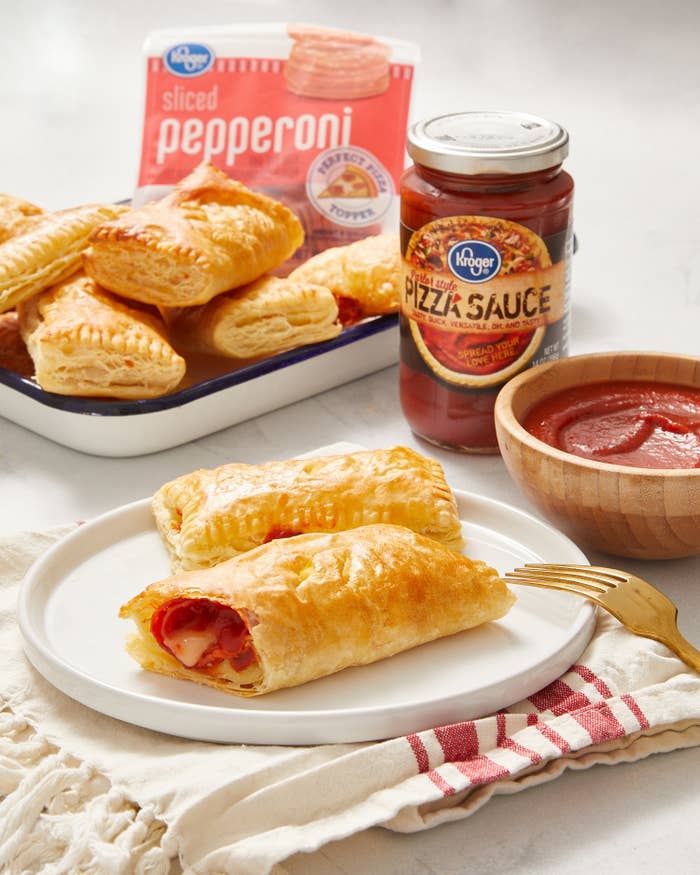 Two pizza puffs served on a plate with a bowl of marinara sauce in the background for dipping