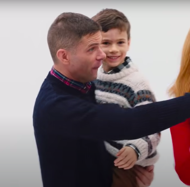 Mikey holds his son, who&#x27;s wearing an itchy Christmas sweater