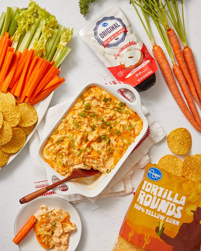 Baking dish filled with buffalo chicken dip and a plate with tortilla chips and celery sticks and carrot sticks