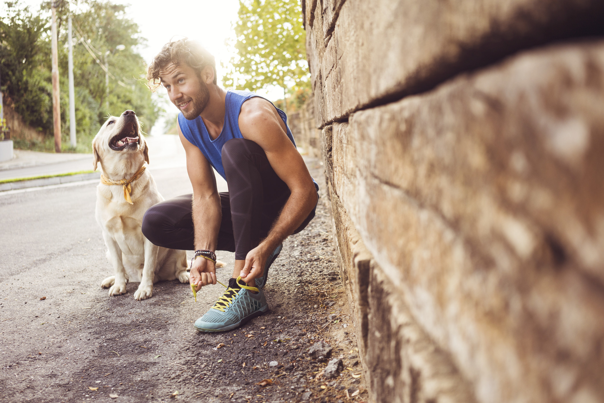 man tying his shoes on an outdoor run with big retriever beside him