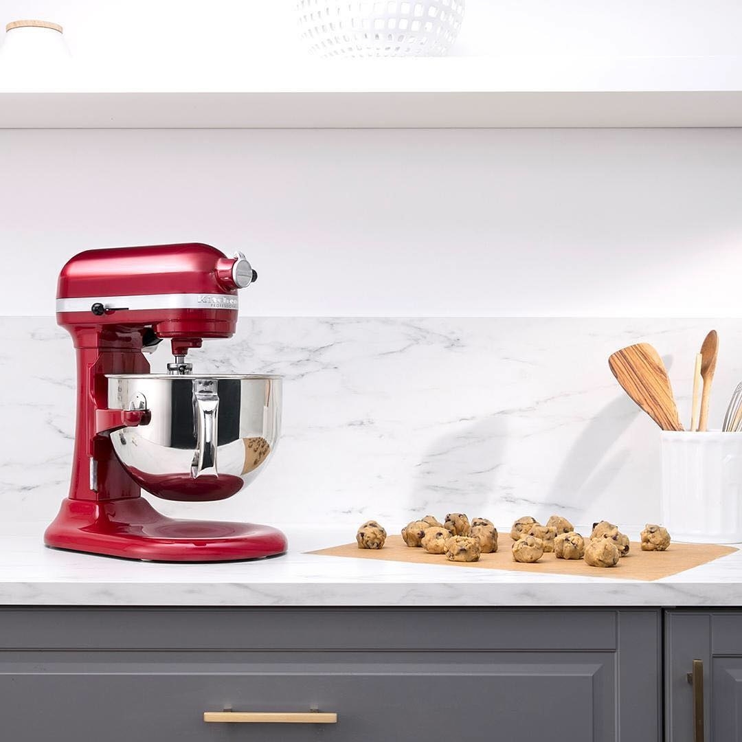 A large stand mixer on a counter top with unbaked cookies on a sheet of parchment paper next to it