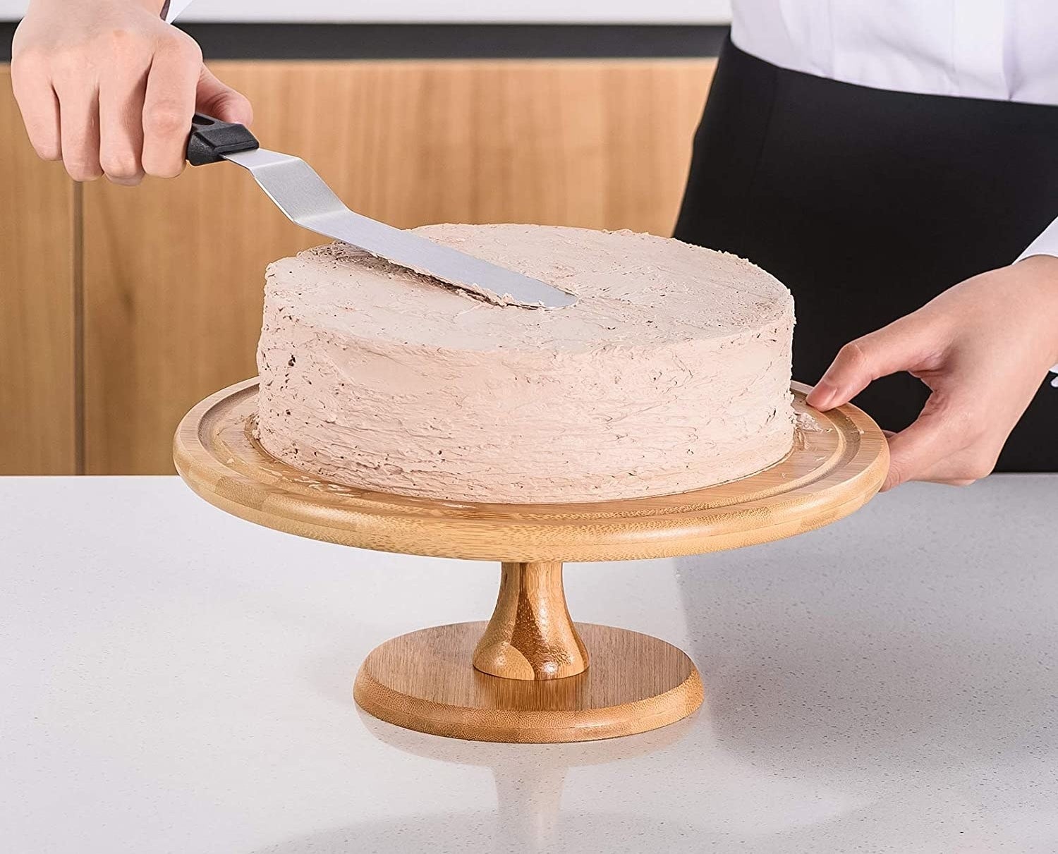 A person icing a cake with a metal spatula