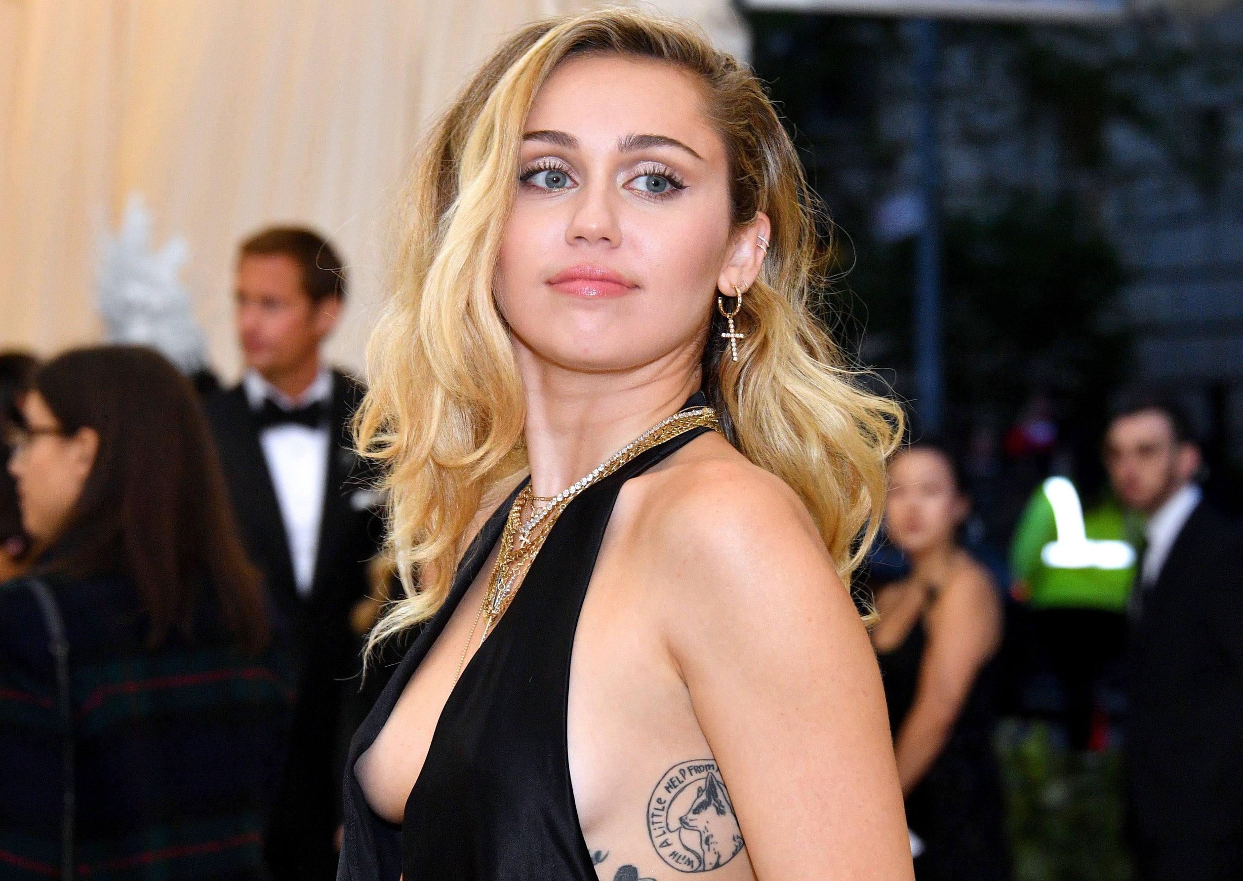 Miley looks over her shoulder while wearing a black dress with a plunging neckline