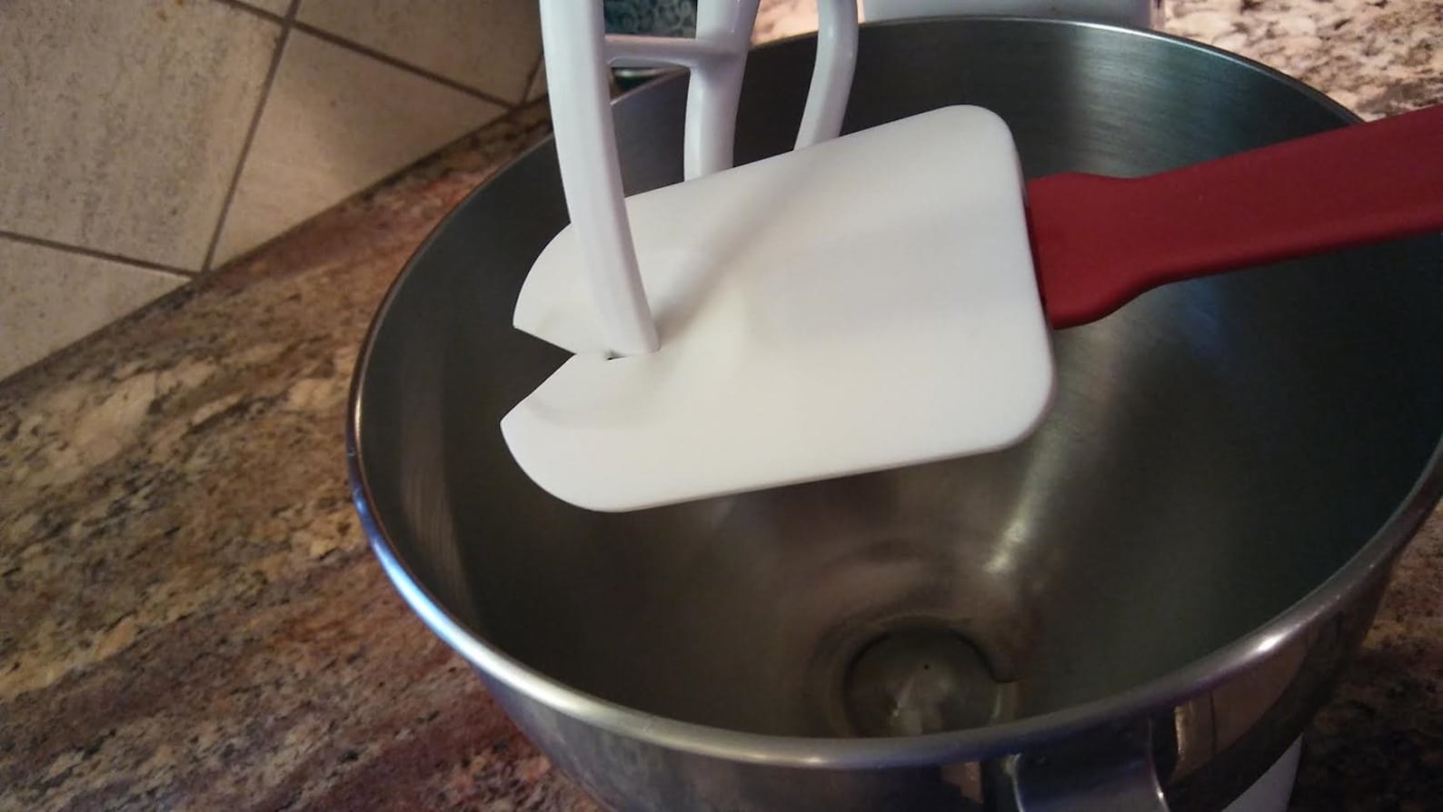 The white spatula cleaning a stand mixer beater attachment