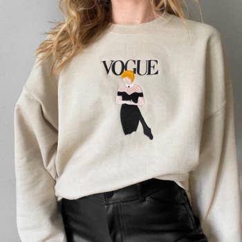 The beige sweatshirt with an embroidered illustration of Princess Diana in a strapless black dress on the front and the word 