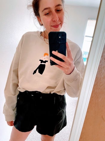 The writer wearing the beige sweatshirt with an embroidered illustration of Princess Diana in a strapless black dress on the front