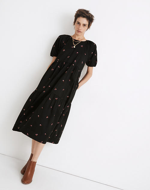 Model is wearing a black floral tiered dress with brown boots