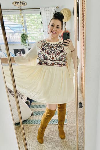 A reviewer wearing the white bell-sleeve dress with colorful embroidery on the bodice